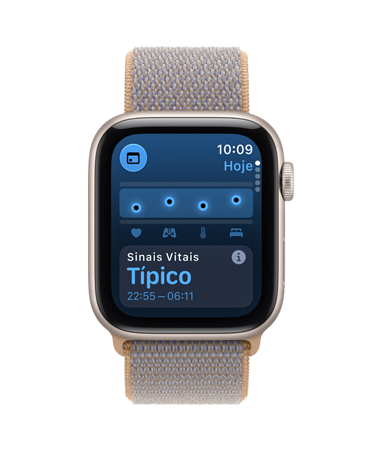 Apple Watch SE 3 com caixa estelar de alumínio e pulseira loop esportiva na cor azul-chambray (azul-acinzentado-claro). A tela mostra o app Saúde (sinais vitais). No lado direito, a Digital Crown.