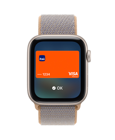 Apple Watch SE 3 com caixa estelar de alumínio e pulseira loop esportiva azul-chambray (azul-acinzentada). A tela mostra o app Carteira e o logotipo de um cartão de pagamento e a Digital Crown aparece na lateral direita