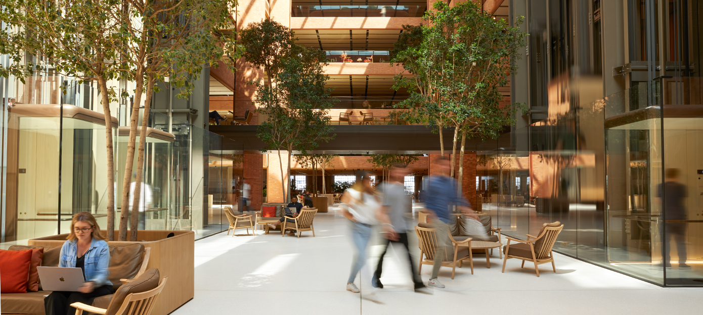La planta baja del luminoso atrio de Battersea, con varias personas del equipo de Apple reunidas, paseando y trabajando en distintas disposiciones de asientos.