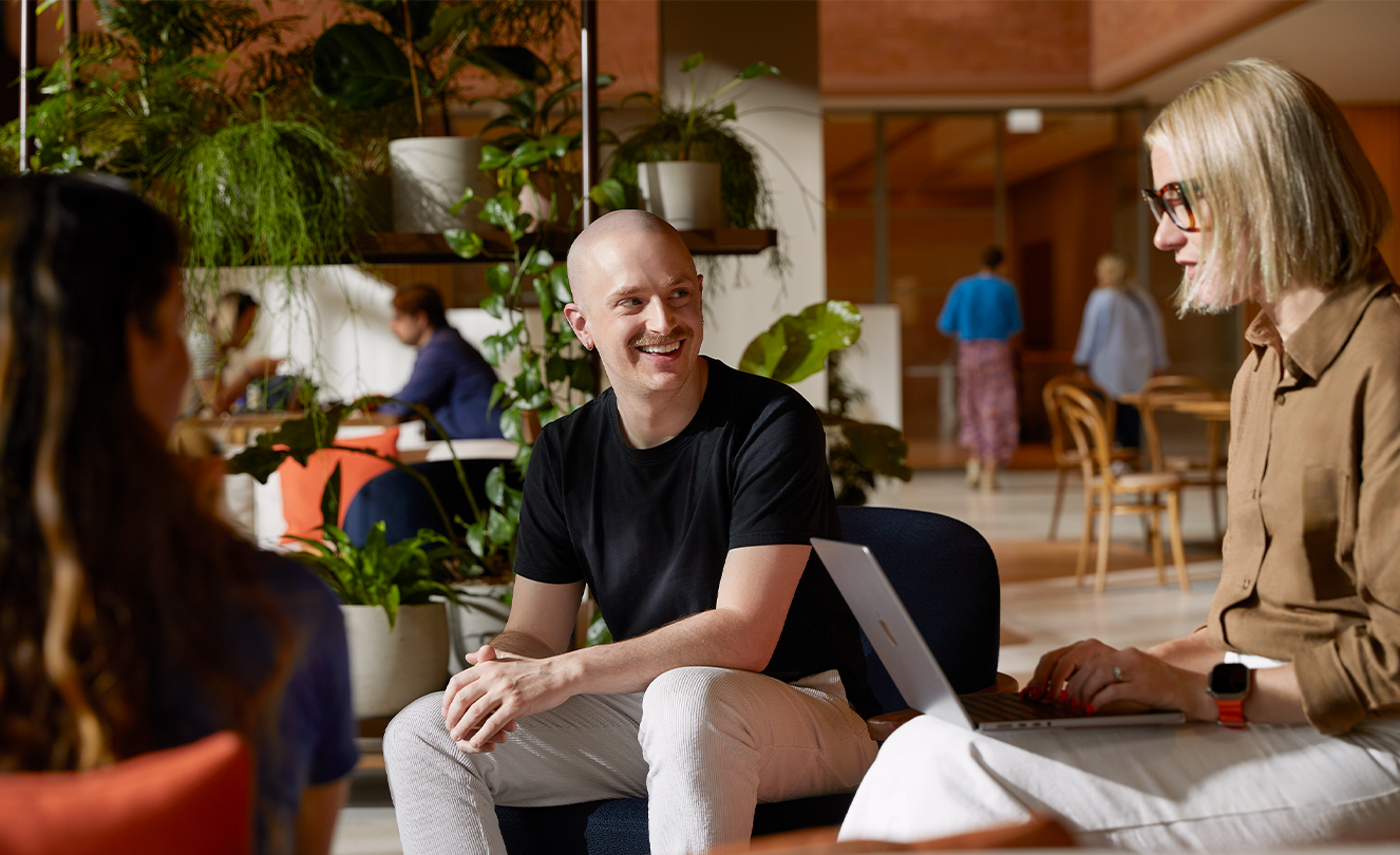 Tres personas del equipo de Apple, una de ellas con una MacBook, conversan mientras están sentadas en los sillones del Caffè Macs.
