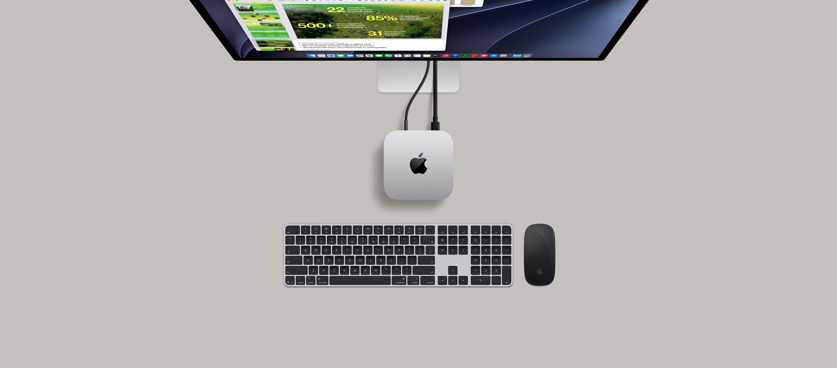 Mac mini felülnézetből, ezüstszínű alumíniumházzal, lekerekített sarkokkal, középen fényes fekete Apple-logóval, kábellel csatlakoztatva, a képen felül egy Studio Display egy része, kinyitott fedelű AirPods 4, Pantone-színminták, piros Logitech billentyűzet és egér