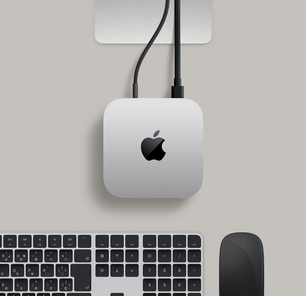 Mac miniを上から見た図。シルバーアルミニウム、丸みを帯びた四隅、中央に光沢のあるブラックのAppleのロゴ、Studio Displayのスタンドが一部見えている。Touch ID搭載Magic Keyboard、Magic Trackpad