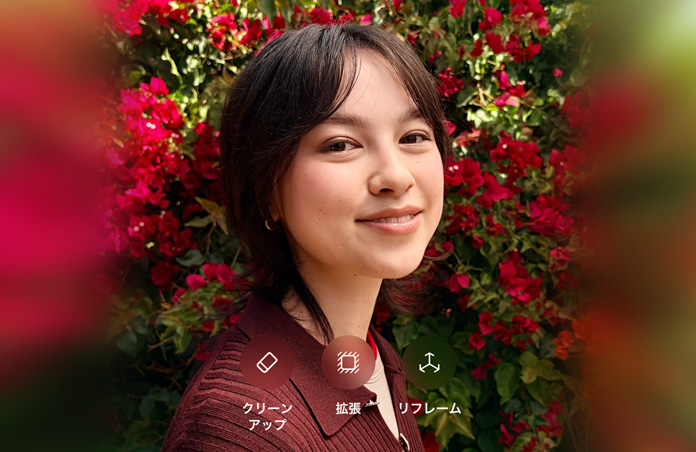茶髪の人物が微笑んでいる写真。茶色のセーターを着て、赤い花に囲まれている。写真上に表示されている「クリーンアップ」「拡張」「リフレーム」のオプションを使ったAIによる写真編集を示している