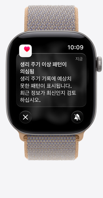 스페이스 그레이 색상 알루미늄 케이스의 Apple Watch Series 12. ‘건강’ 앱의 생리 주기 추적에 ‘생리량 있음, 경련성 복통 및 그 외 2개’ 알림이 표시되어 있으며, 샴브레이 블루(연한 블루 그레이) 색상 스포츠 루프 밴드를 장착