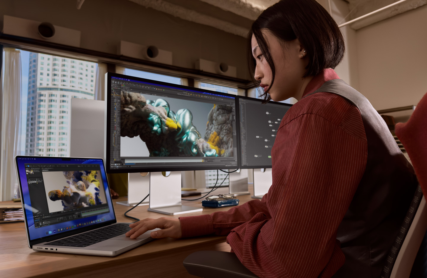 سيدة في مكتب تعمل على لابتوب MacBook متصل بشاشة Studio Display XDR عبر منفذ ثندربولت 5