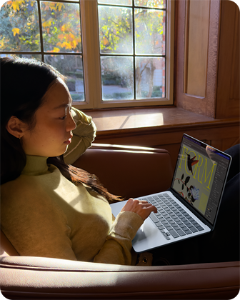 O persoană stă pe un scaun și folosește un MacBook Air