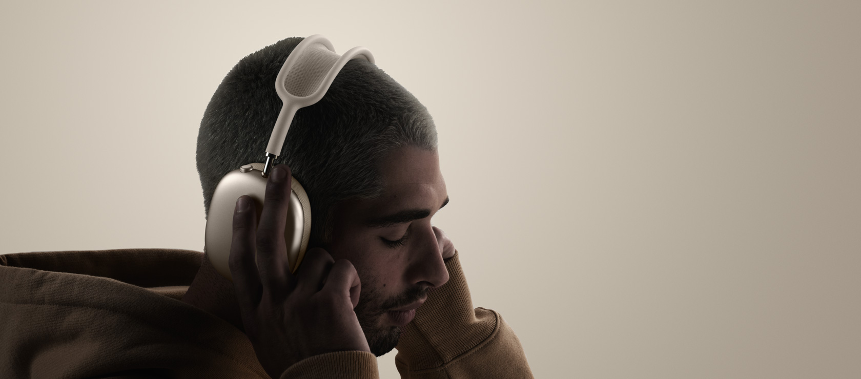 Persona ir uzlikusi AirPods Max 2 austiņas, sānskats, pieskaras austiņu spilventiņiem