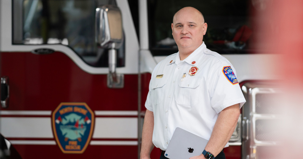 Le chef des pompiers se tient devant un camion de pompiers avec un iPad à la main et une Apple Watch au poignet