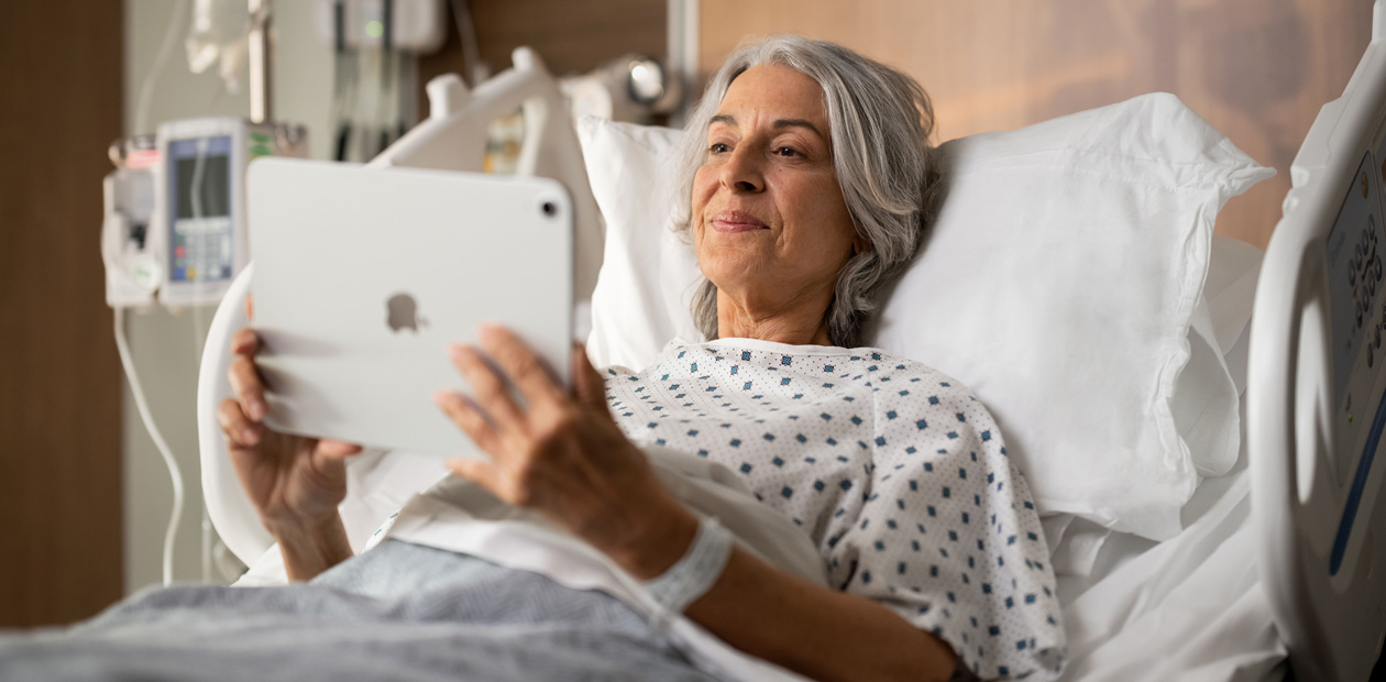 Une patiente, allongée sur un lit d’hôpital, regarde son iPad.
