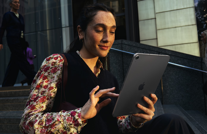 Eine Person sitzt auf Stufen vor einem grossen Gebäude und nutzt ein 11 Zoll iPad Air in Space Grau mit nahtloser WLAN Verbindung während der Datenübertragung